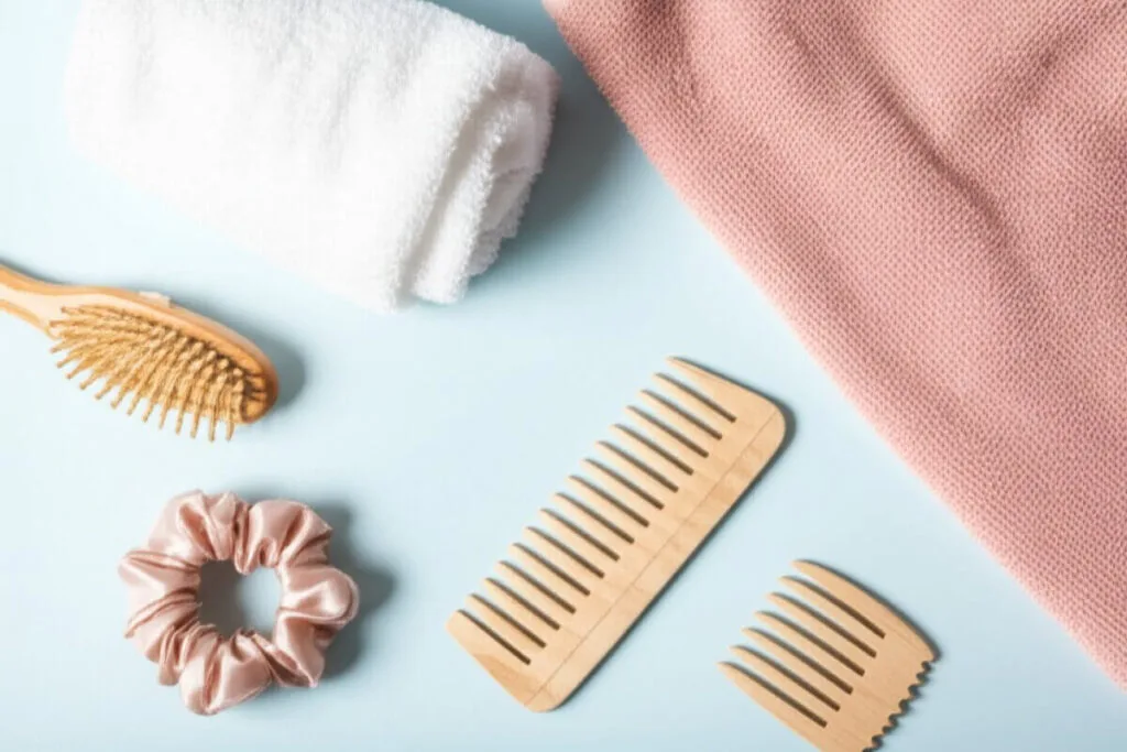 Utensilien für eine sanfte Haarpflege-Routine zur Vorbeugung von Haarausfall bei Frauen: Holzbürste, breitzinkiger Kamm und Mikrofaserhandtuch.